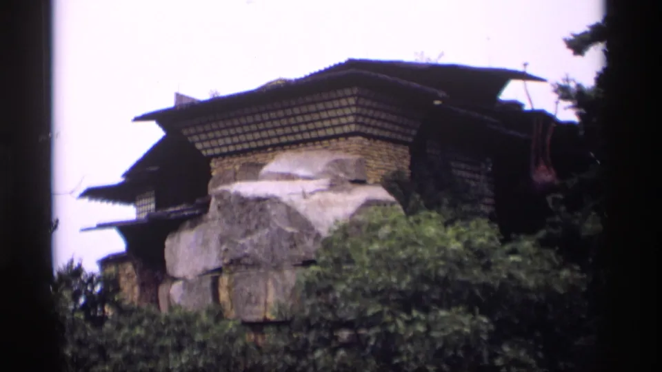 1969 Wisconsin 8mm frame showing a Japanese-style tiered-roof structure set into large rock formations with surrounding greenery.