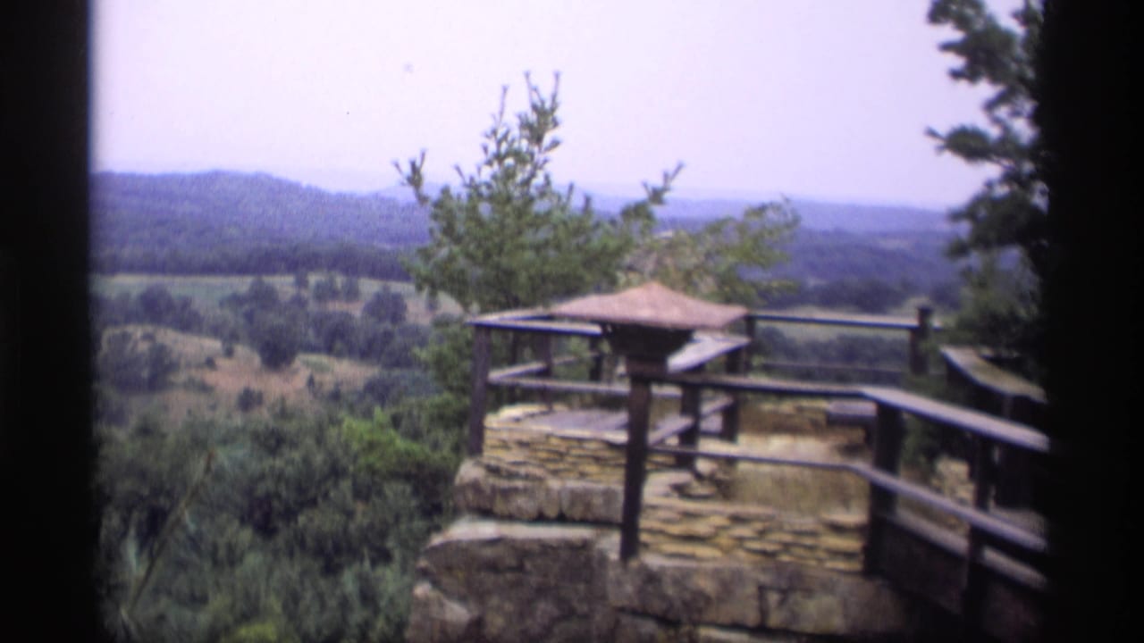 Stone overlook platform with wooden railing above wooded hills.