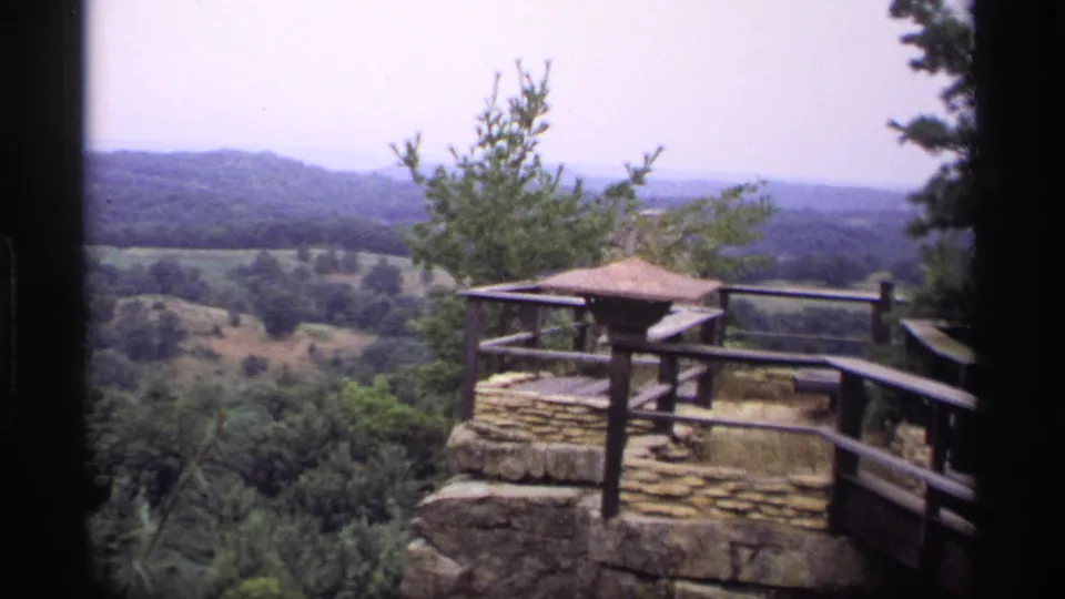 1969 Wisconsin 8mm frame showing the same stone-and-wood overlook against a soft, distant view of forested ridges.