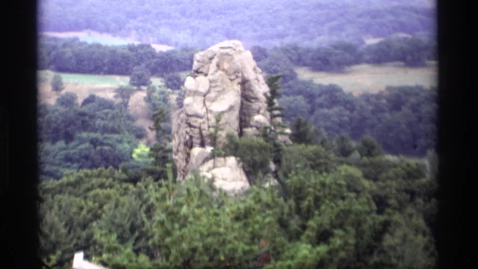 1969 Wisconsin 8mm frame with a rugged rock formation above forest canopy and muted rural hills beyond.
