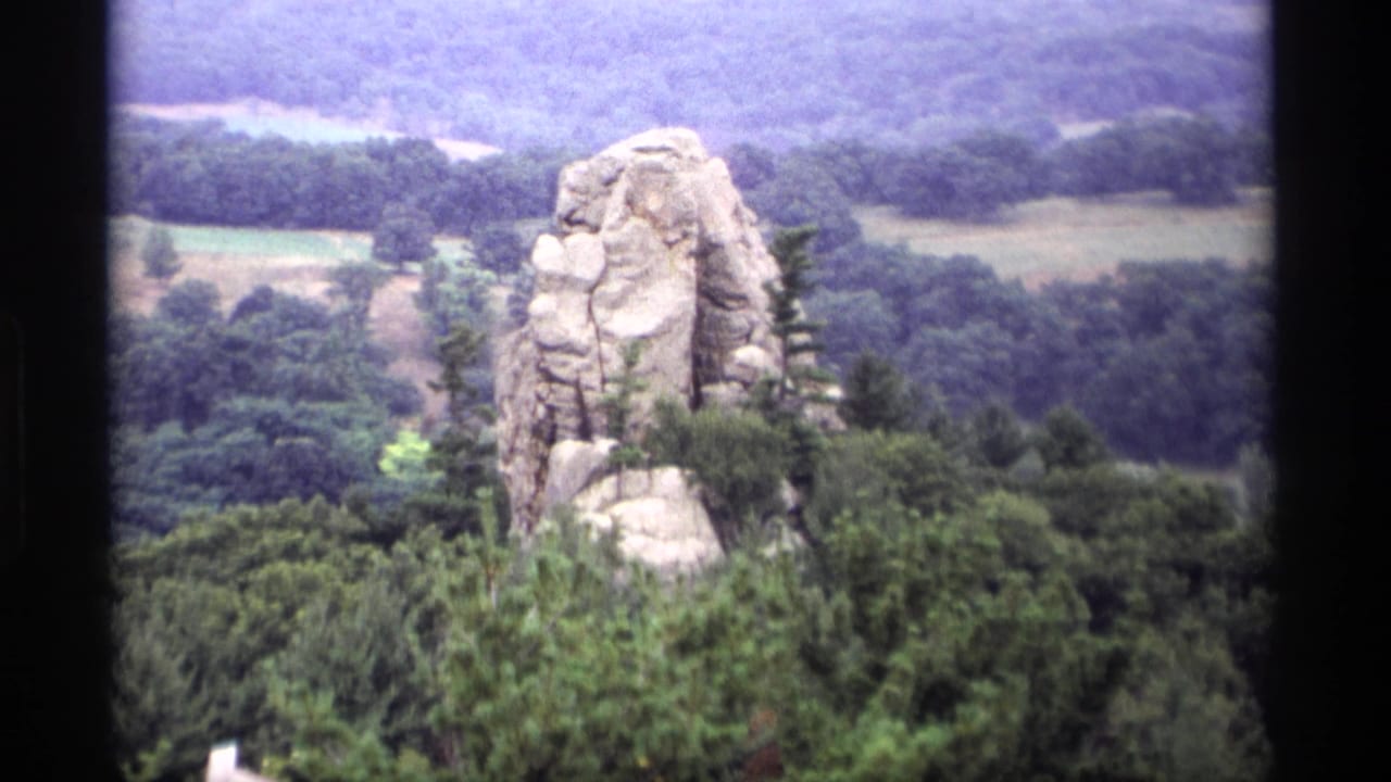 1969 Wisconsin 8mm frame showing a tall rock outcrop above wooded hills and pale fields in the distance.
