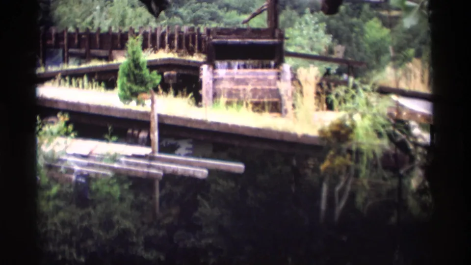 1969 Wisconsin 8mm frame showing the waterwheel area with a partially obscured building on a wooded hillside.