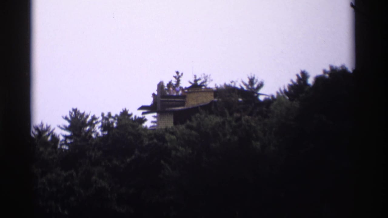 Distant hilltop structure partly hidden by evergreen trees under a pale sky.