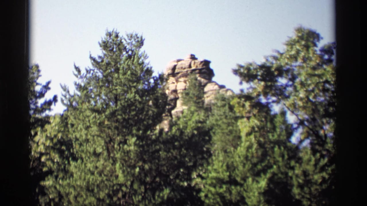 Sandstone rock formation rising above green trees under a blue sky.