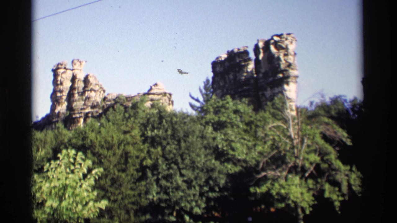 1969 Wisconsin home-movie frame with several sandstone towers seen over leafy trees and open sky.