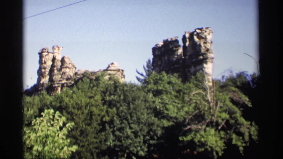 Vintage 8mm Wisconsin landscape frame showing sandstone formations behind thick green foliage.