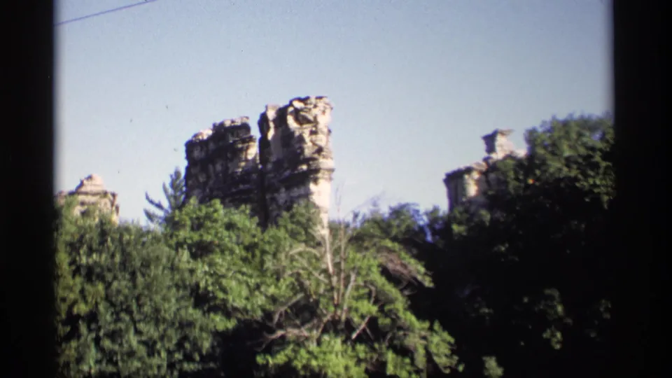 1969 Wisconsin 8mm frame showing pale, weathered rock formations above a leafy tree canopy beneath clear sky.