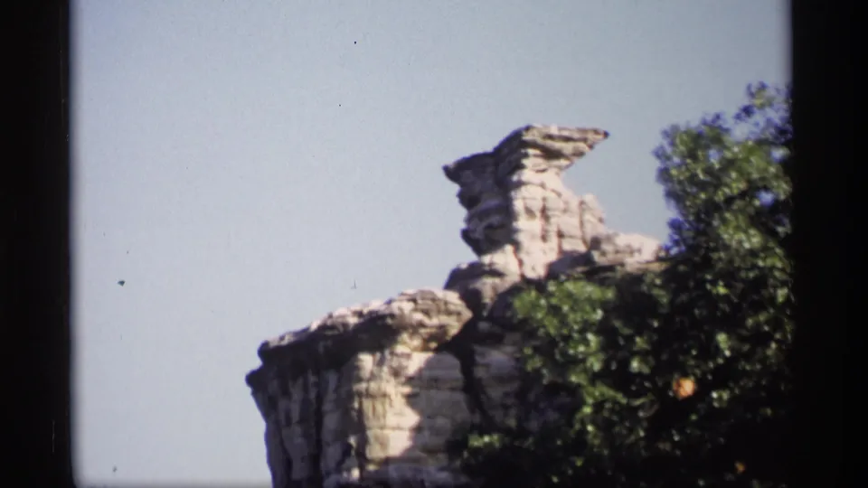 1969 Wisconsin home-movie frame with a closer look at a stacked rock outcrop and nearby leafy trees.