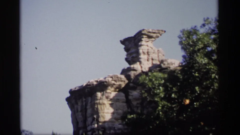 1969 Wisconsin 8mm frame showing a prominent layered rock formation rising above the wooded canopy.