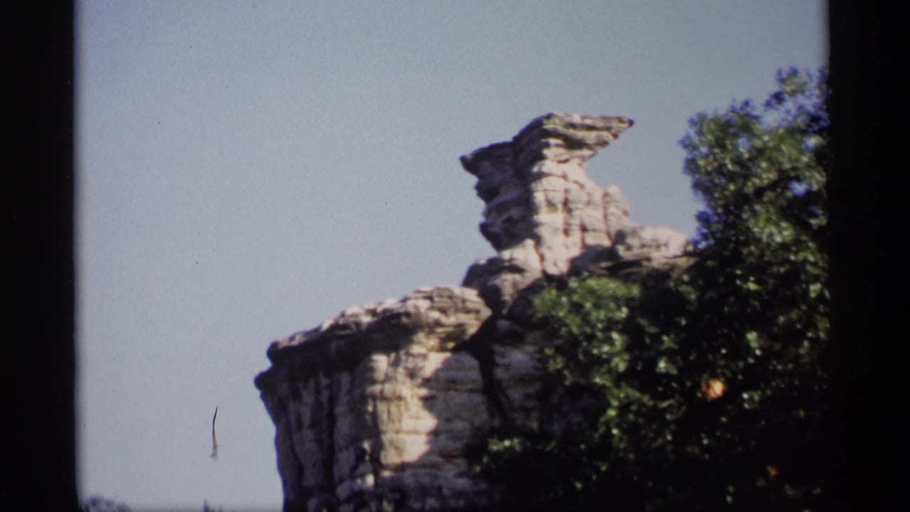 1969 Wisconsin 8mm frame showing a pale rock formation above leafy trees, with blue sky and visible film gate edges.