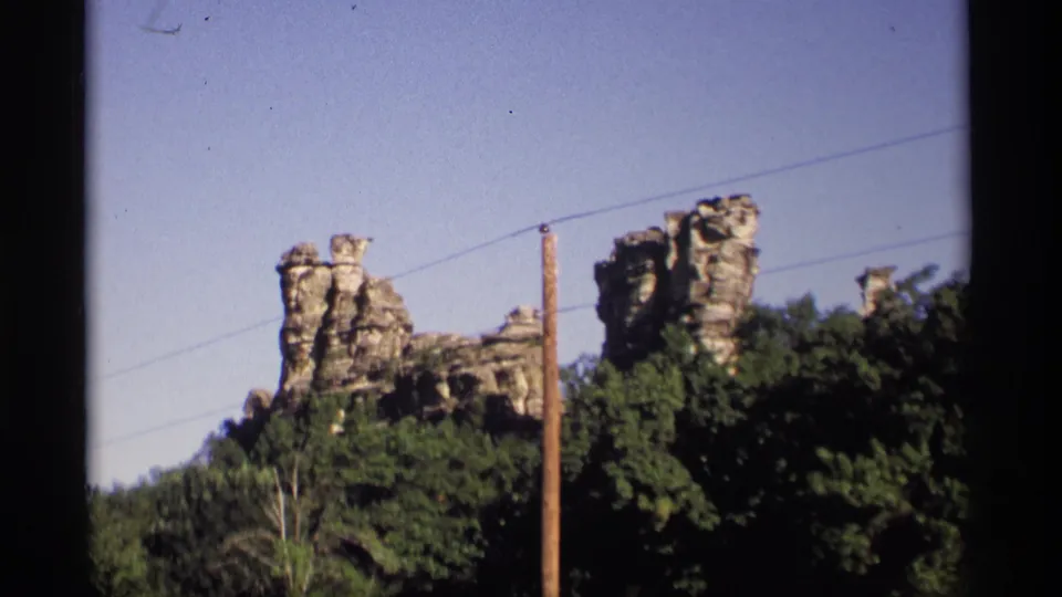 1969 Wisconsin 8mm frame with pale rock outcrops, dense trees, a utility pole, and overhead wires.