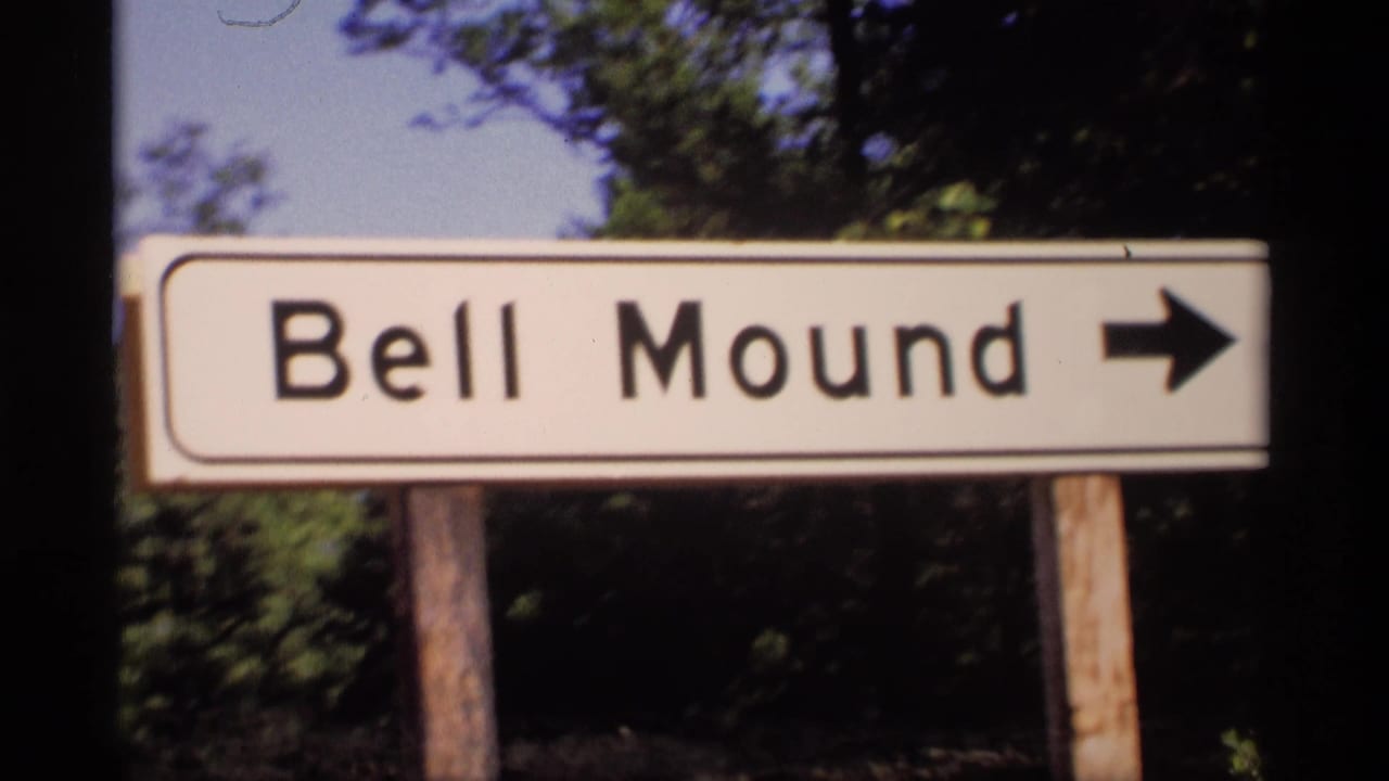 The Bell Mound sign remains centered in a 1969 Wisconsin home-movie frame, with a black arrow pointing right and trees behind it.
