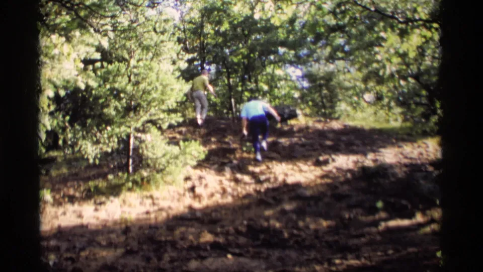 Two people climb a sunlit wooded hillside in Wisconsin, seen from a handheld 8mm home-movie viewpoint.