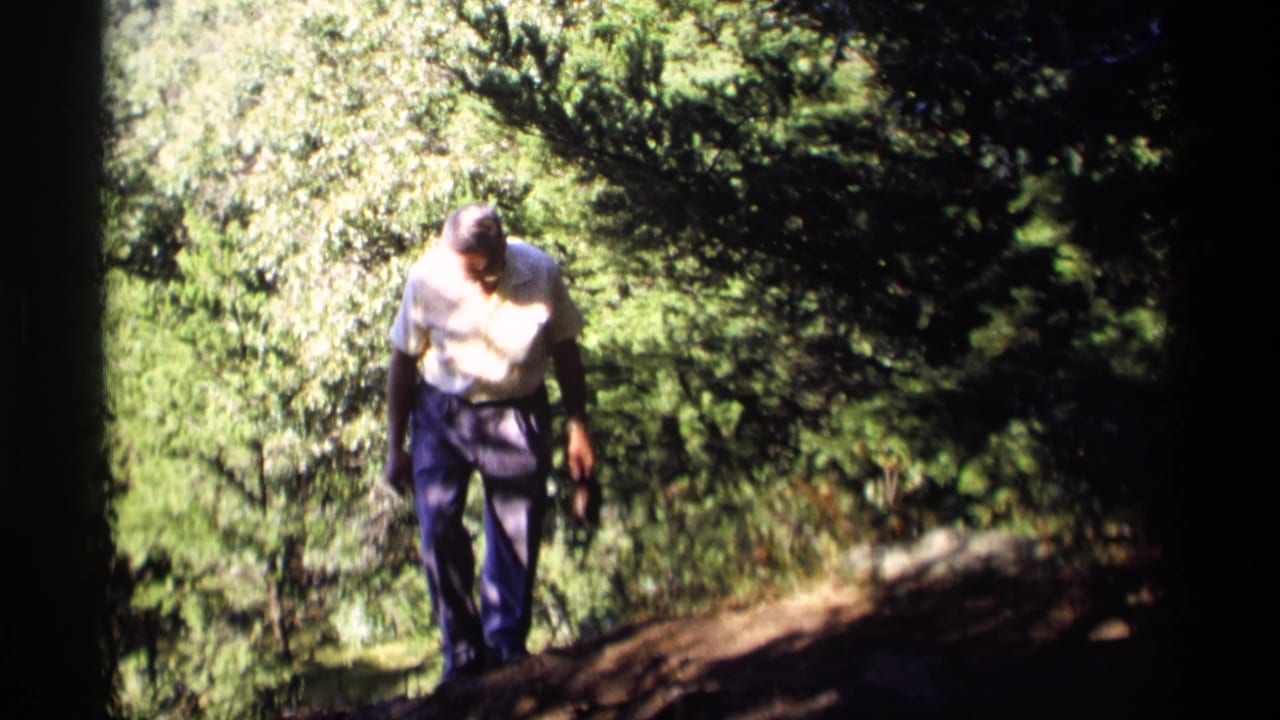 Older man looks down while walking along the wooded trail.