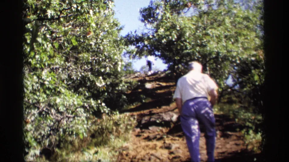 The closing frame shows the man leaning into the climb on a rocky Wisconsin hillside, surrounded by dense green foliage and bright daylight.