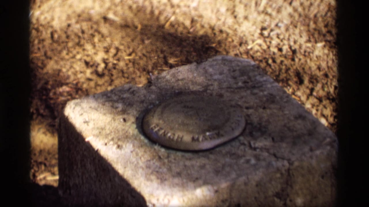 Round metal bench mark set into a weathered stone pedestal outdoors.