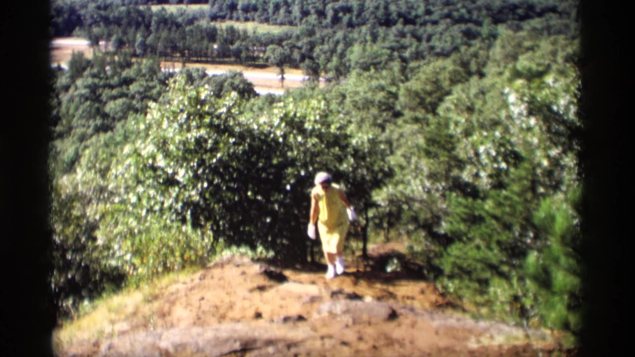 Woman in a yellow dress walking on a wooded hillside path.