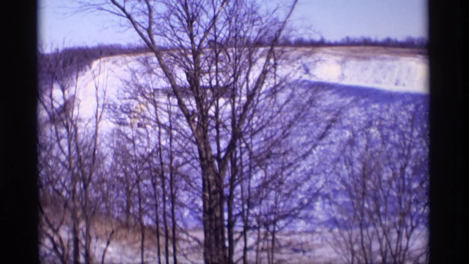 A wide winter view shows bare trees in the foreground and a snow-dusted Wisconsin hillside beyond, filmed on 8mm in 1969.