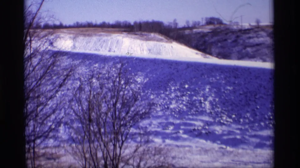 1969 Wisconsin 8mm frame showing a bright snowy field, low hill, bare trees, and distant horizon structures.