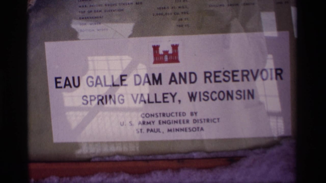 1969 Wisconsin 8mm frame showing the Eau Galle Dam and Reservoir sign for Spring Valley, with reflections across the glass.
