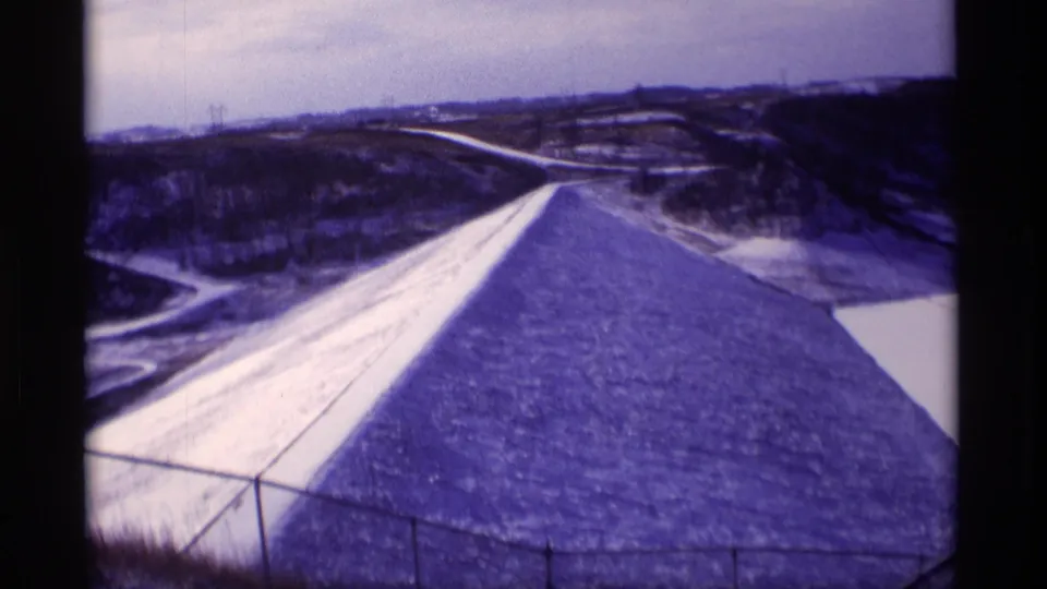 1969 Wisconsin 8mm frame holding on the Eau Galle Dam structure, with the sloped surface leading toward roads and hills.