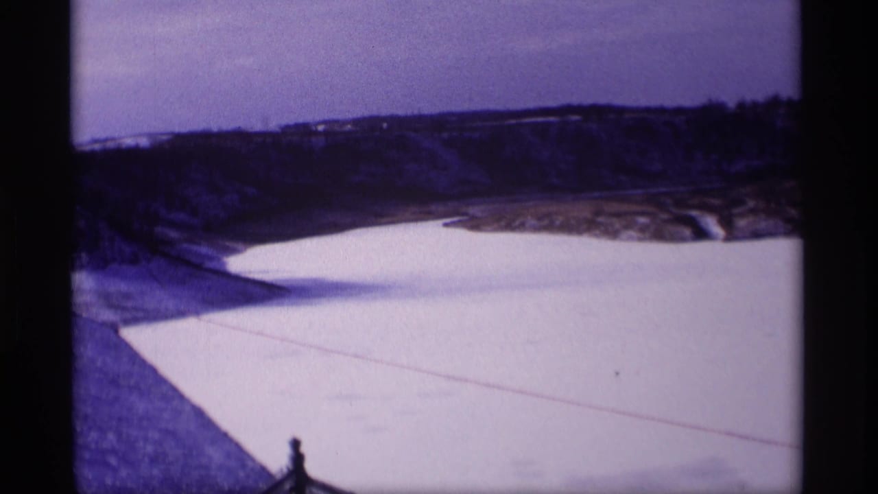 Snow-covered dam or embankment beside a frozen reservoir with distant hills.