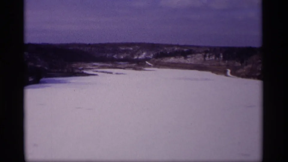 1969 Wisconsin winter landscape showing a frozen reservoir, low wooded hills, and a winding far shoreline in soft 8mm color.