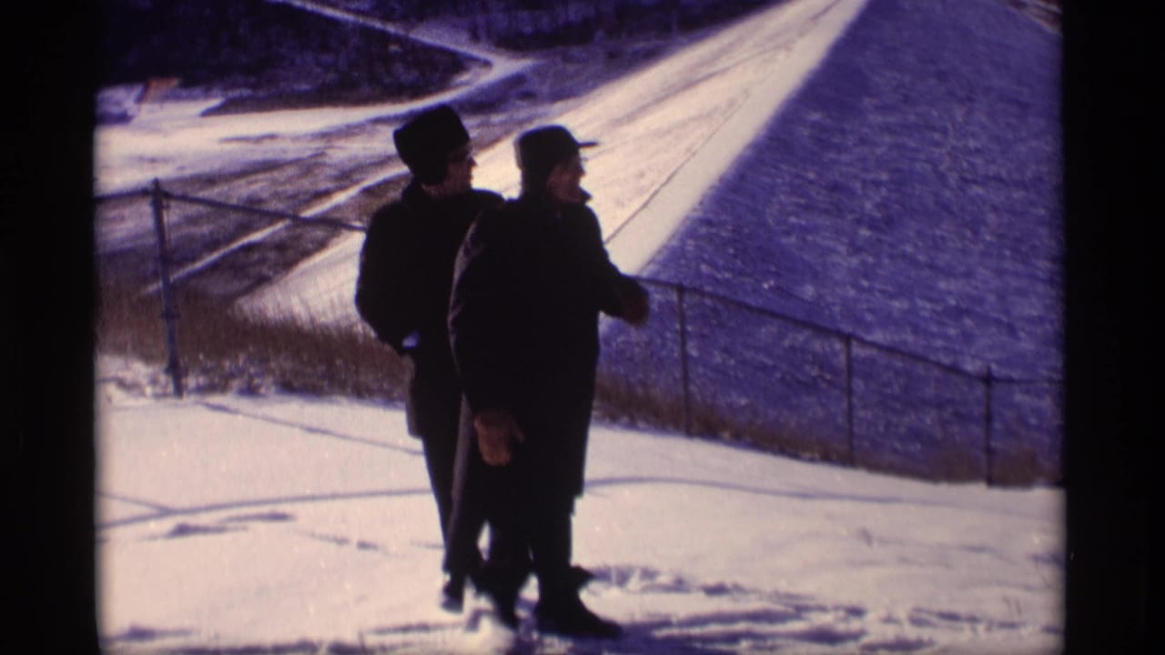 Two bundled men pass each other near a snow-covered levee slope and railing.