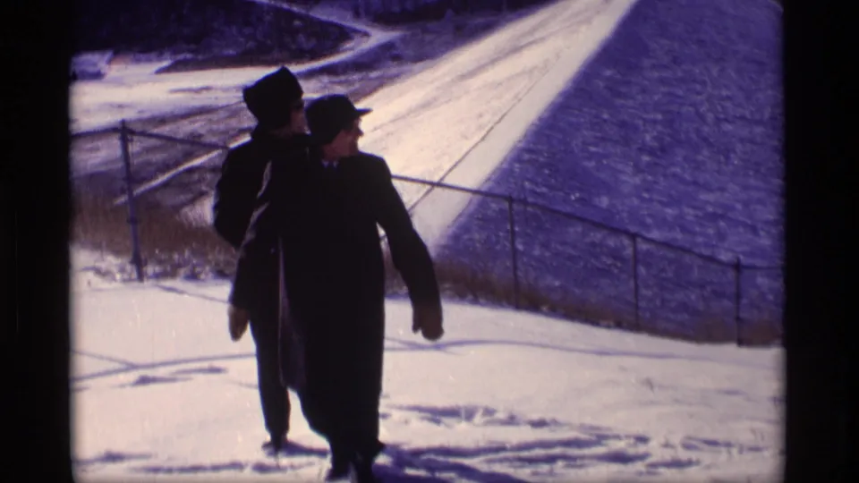 Two adult men in dark winter clothing walk toward the camera on snow beside a levee railing in the Wisconsin winter scene.