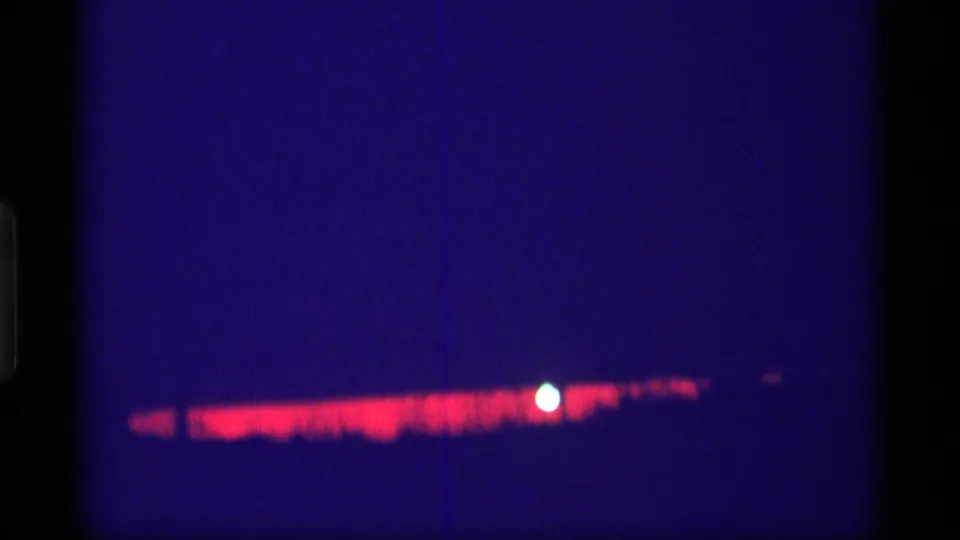 8mm night frame from the Wisconsin 1969 clip showing a red horizontal glow under a deep blue field with a small bright orb.