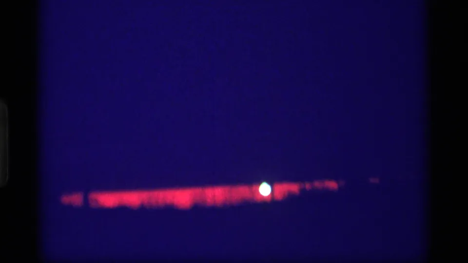 8mm night frame from the 1969 Wisconsin footage with a red band of light and a small white orb against deep blue darkness.