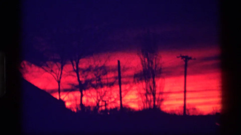 1969 Wisconsin 8mm frame with utility poles, bare trees, and a dark sloping horizon silhouetted against a red-magenta sunset.