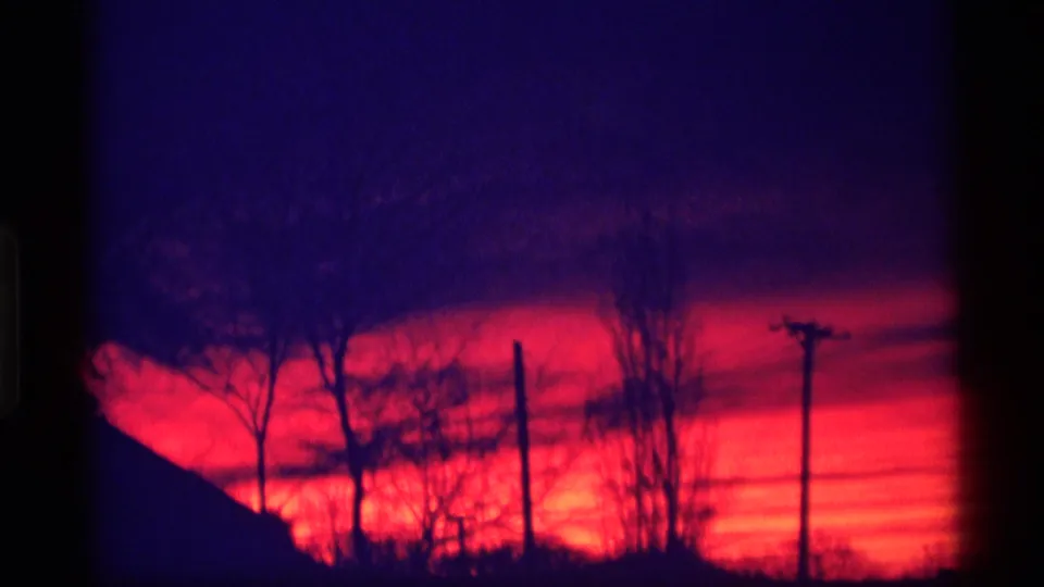 1969 Wisconsin 8mm frame showing a low dark hill or roofline, utility poles, and bare trees under a red-purple evening sky.
