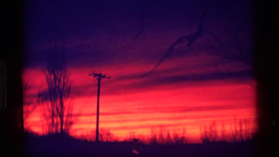 1969 Wisconsin 8mm frame with a utility pole, bare tree silhouettes, brush, and a saturated red sunset fading into purple twilight.