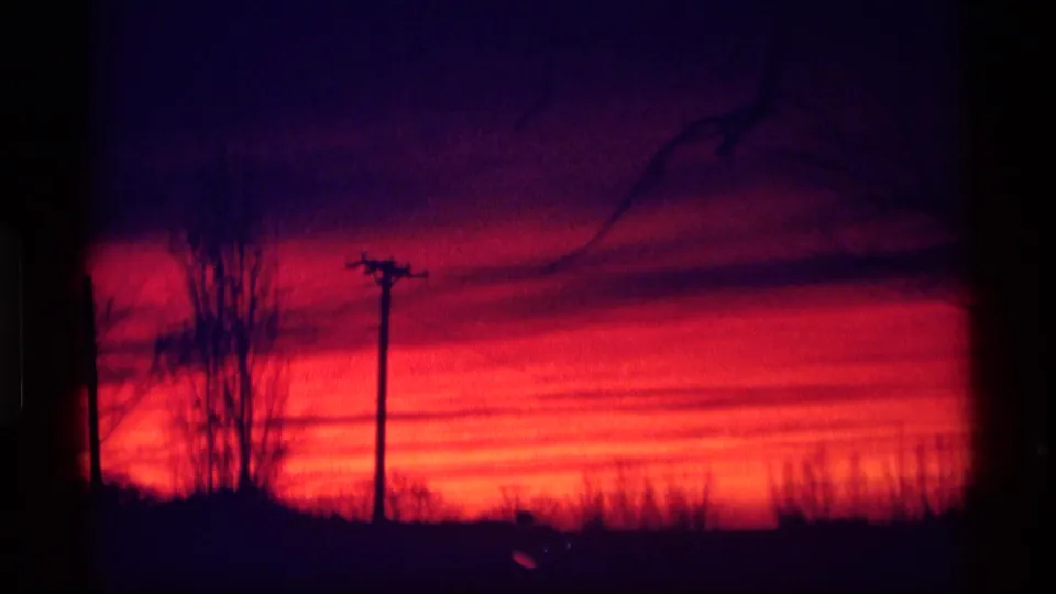 1969 Wisconsin 8mm frame showing a vivid red-purple sunset with tree silhouettes and a utility pole near the horizon.