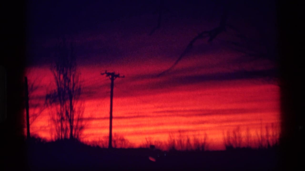 1969 Wisconsin 8mm frame of a saturated red dusk sky, with bare trees and a utility pole in silhouette.