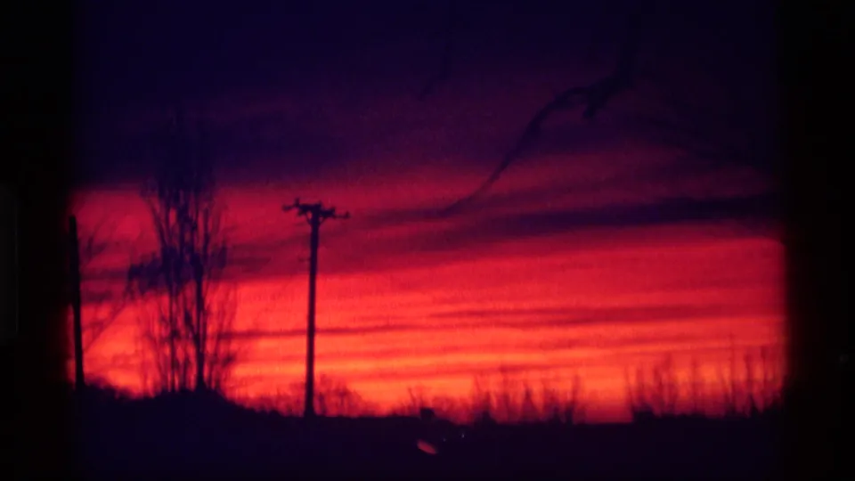 1969 Wisconsin 8mm frame of a saturated red dusk sky, with bare trees and a utility pole in silhouette.