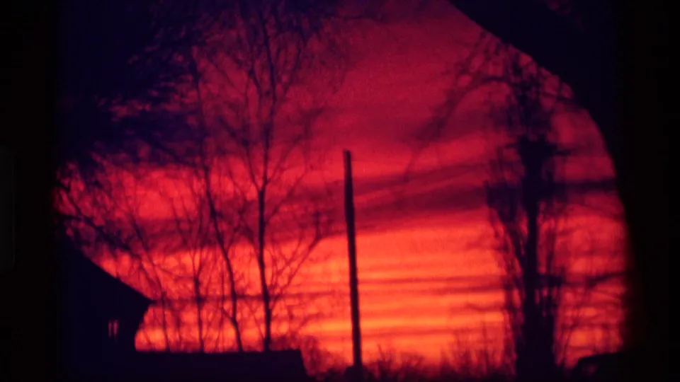 1969 Wisconsin 8mm frame with saturated red and orange sky behind bare trees, a utility pole, and a dark roofline.