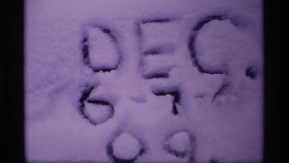 Archival 1969 Wisconsin home-movie frame focused on handwritten snow markings, with visible grain and tinting.