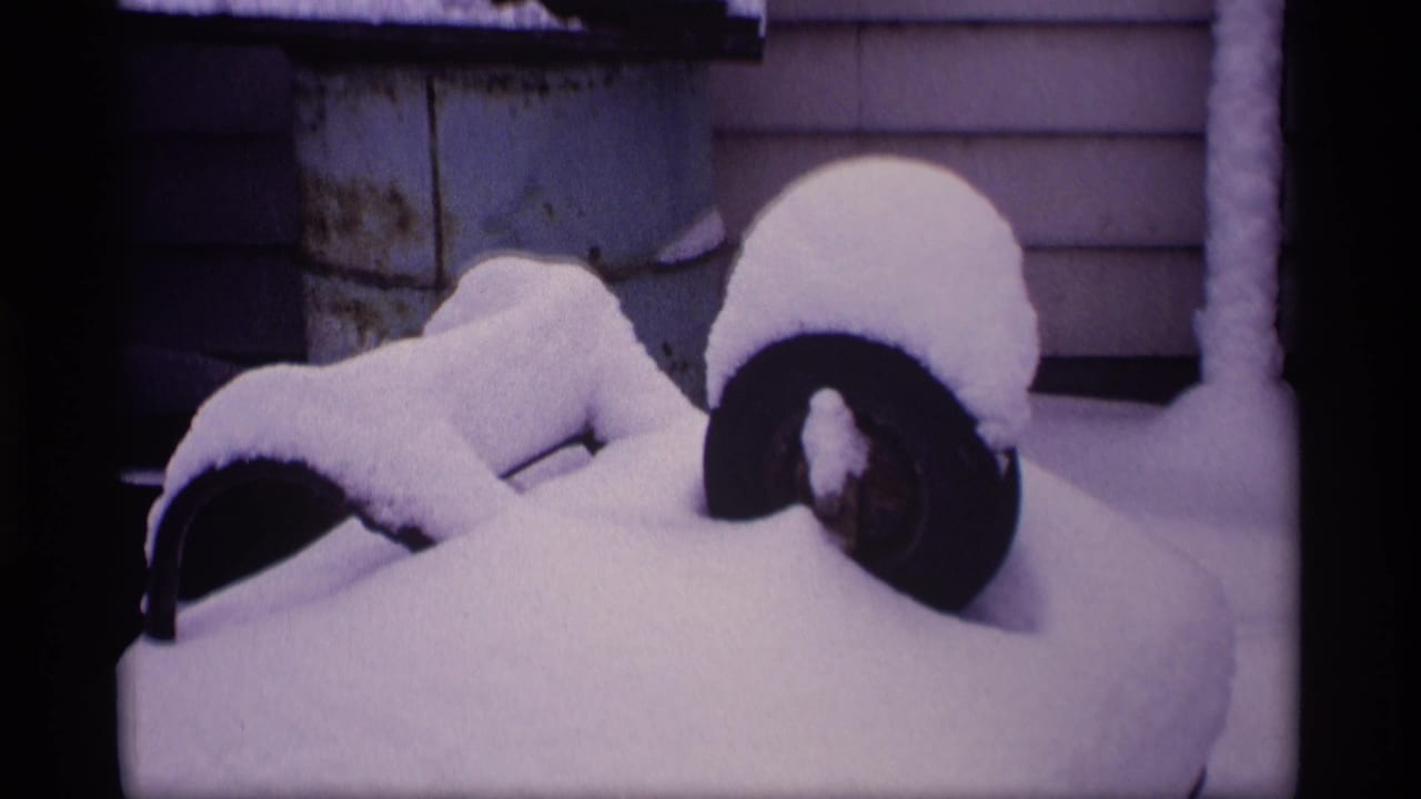 Snow-covered barbecue grill beside house siding in a winter yard.