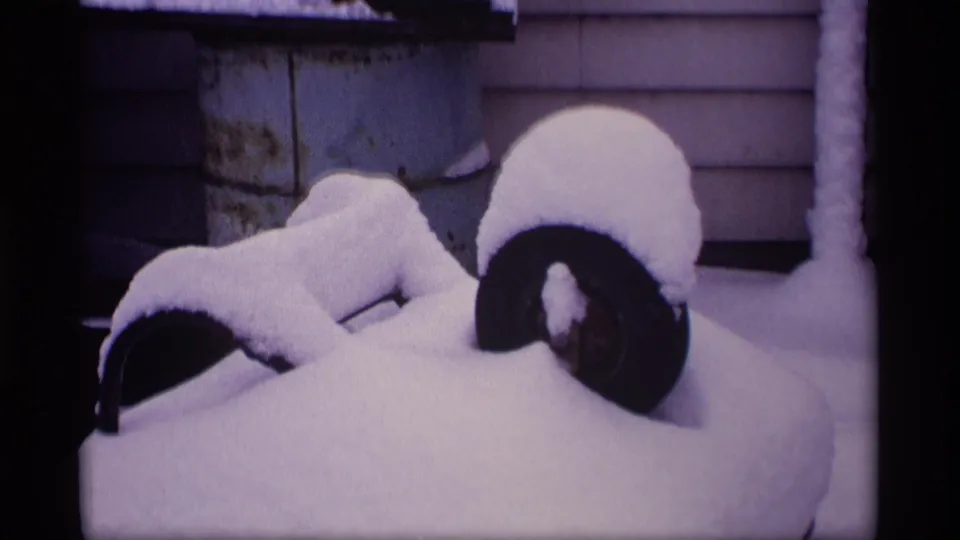 1969 Wisconsin 8mm frame showing a barbecue grill and nearby yard objects buried under heavy snow beside house siding.