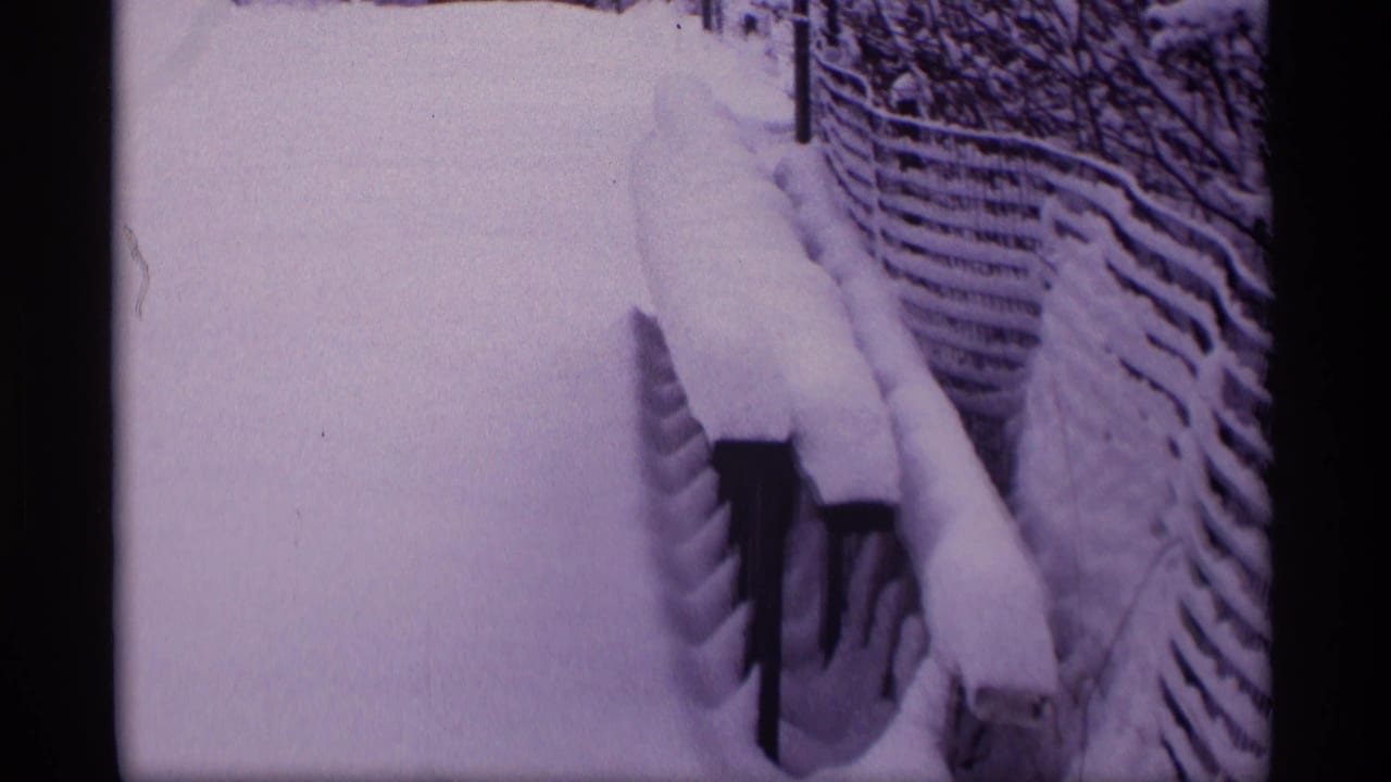 1969 Wisconsin 8mm frame showing a snow-filled yard path bordered by a fence and railings under deep winter accumulation.