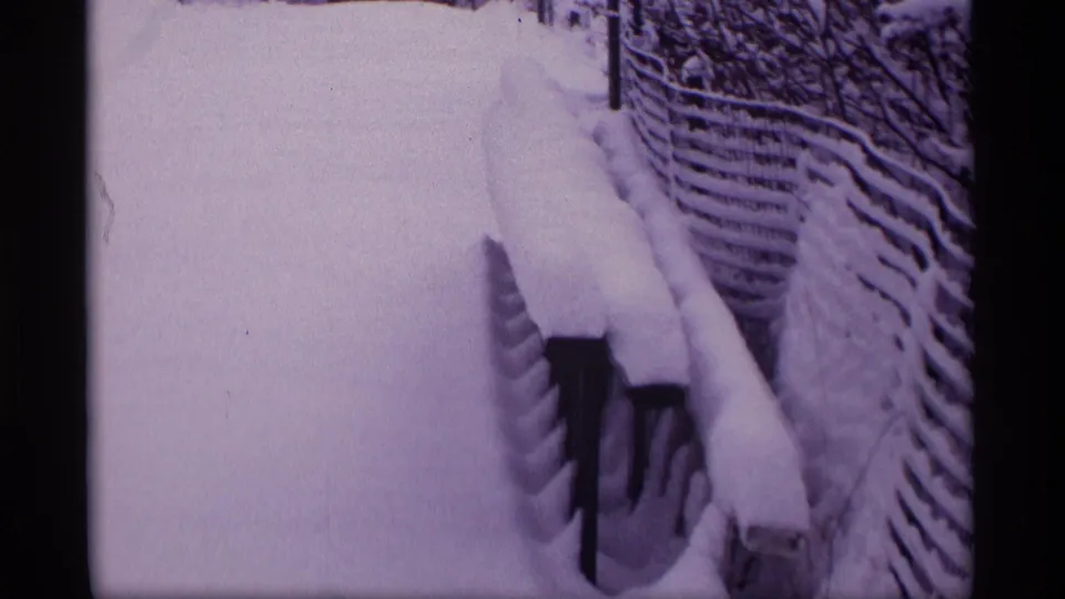 1969 Wisconsin 8mm frame showing a snow-filled yard path bordered by a fence and railings under deep winter accumulation.
