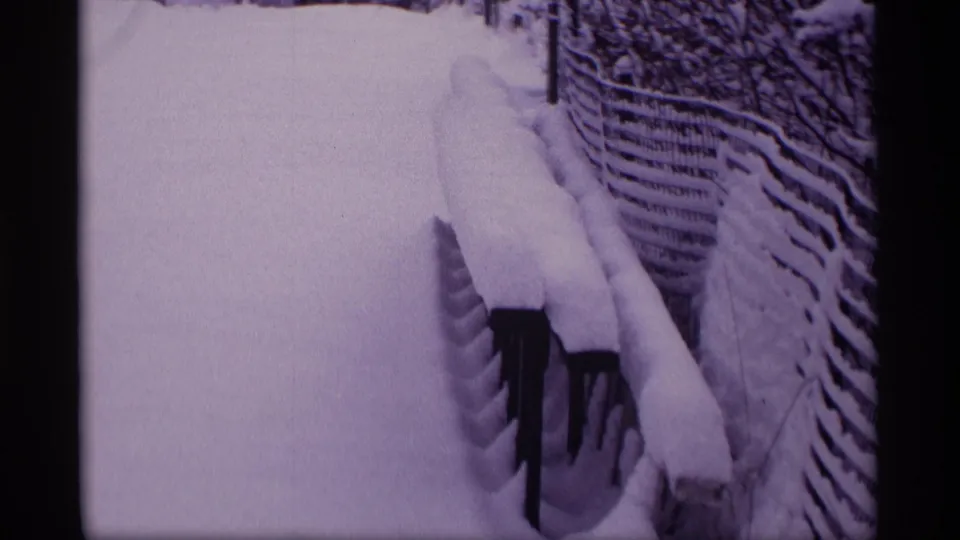 1969 Wisconsin 8mm frame showing a fence line, snowbank, and buried railings along a quiet winter yard path.