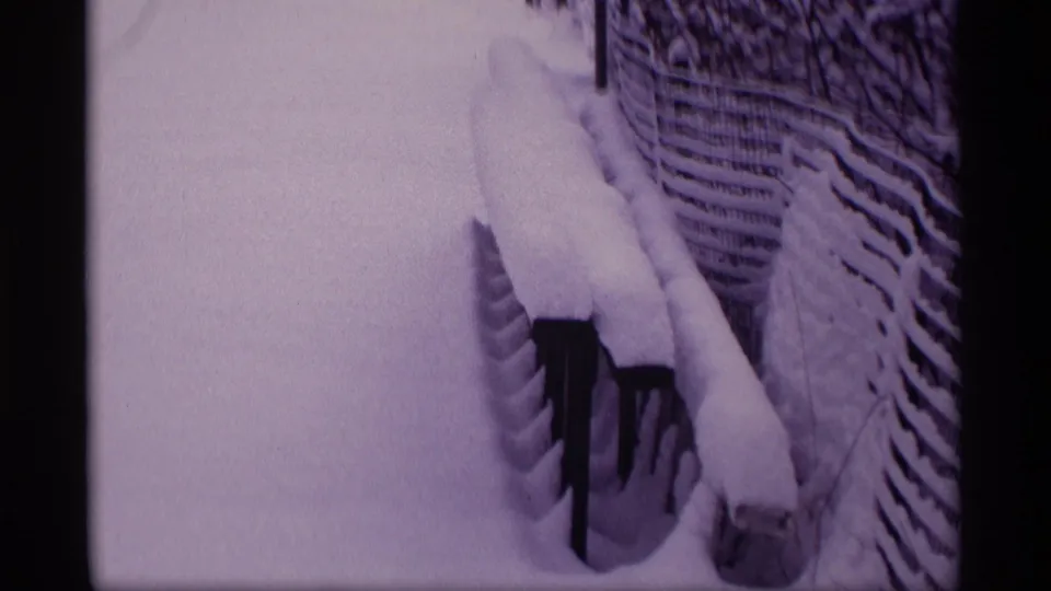 1969 Wisconsin 8mm frame showing snow piled on a wooden fence beside a quiet winter yard.