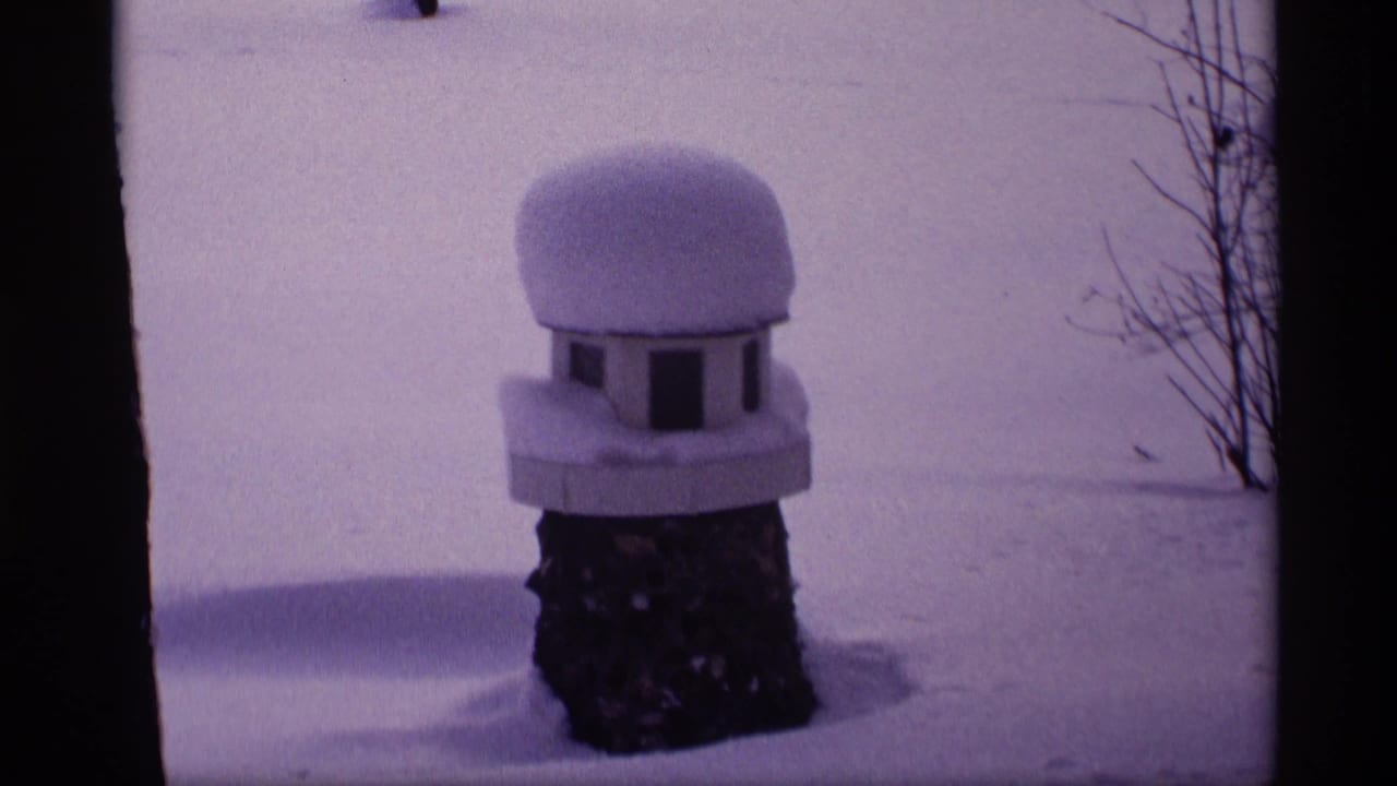 1969 Wisconsin winter frame with a rounded snow cap on a small birdhouse or feeder set against a snowy yard.