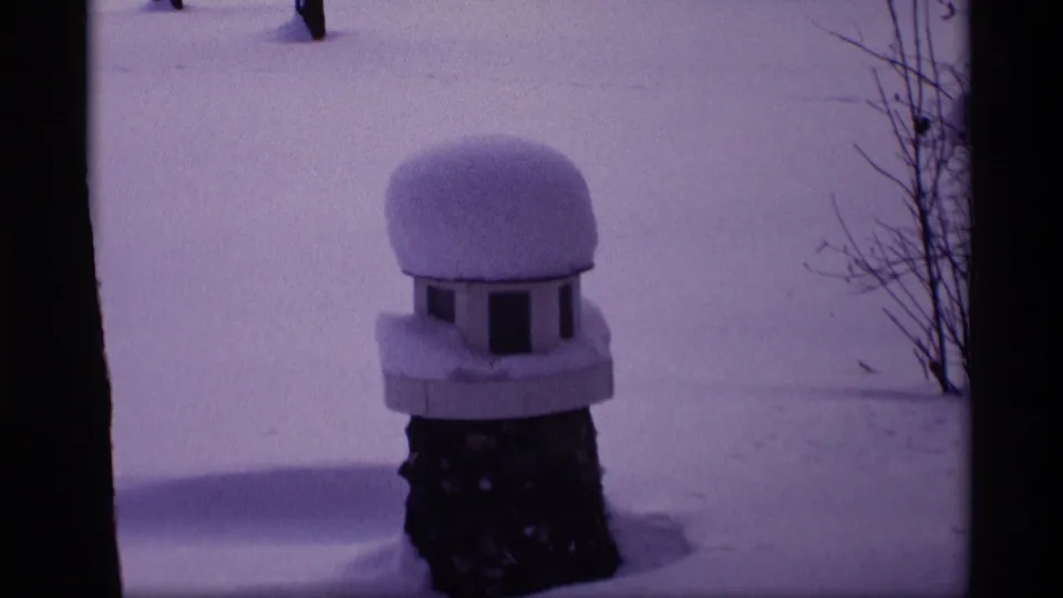 1969 Wisconsin 8mm frame showing a dome-topped birdhouse heavily covered in snow near a quiet residential yard.