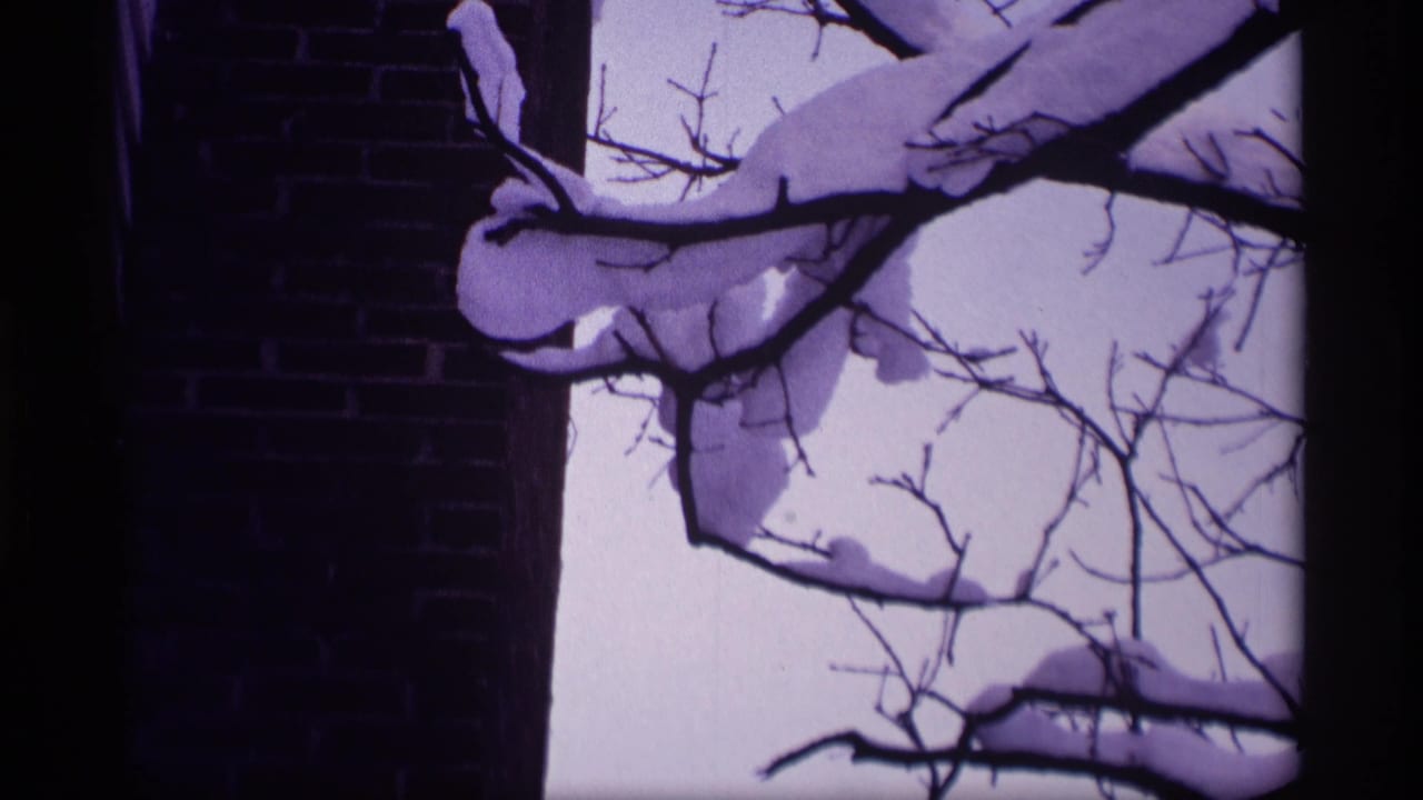 Snowy tree branches crossing a pale sky beside a brick building edge.