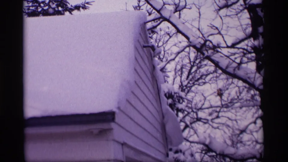 1969 Wisconsin 8mm frame showing a snow-covered residential roof, siding, and winter branches.