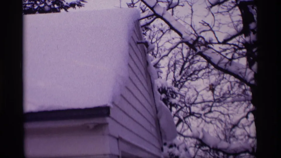 1969 Wisconsin exterior frame with deep roof snow, white siding, and winter branches close to the house.
